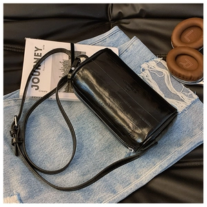 Detail of black cylindrical pillow bag with glossy pleated leather and adjustable strap