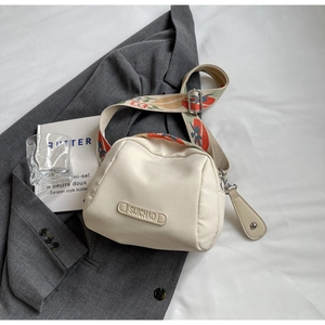 Detail of a creamy white canvas crossbody bag with a colorful floral jacquard strap