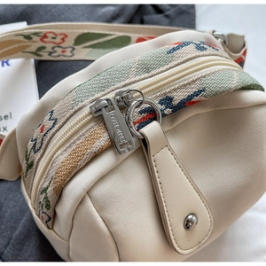 Detail of canvas crossbody bag with floral embroidery strap and silver double zippers
