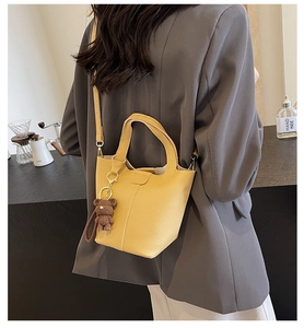 Detail of yellow lychee grain leather bucket bag with a cute bear charm on a grey blazer