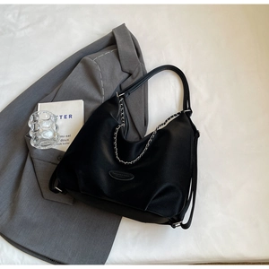 Detail of black leather tote bag with silver chain on grey blazer in a stylish setting