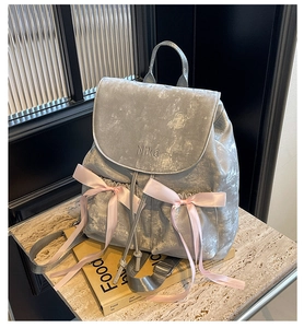 Detail of silver backpack featuring pink satin bows and NiKa embroidery on glossy fabric