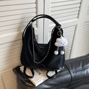 Black lychee leather dumpling bag with silver chain and white fluffy charm on books