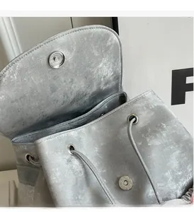 Detail of silver metallic backpack featuring shiny fabric and magnetic snap closure