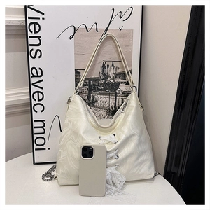 Close-up of cream white shoulder bag with marble texture and lace details beside a phone