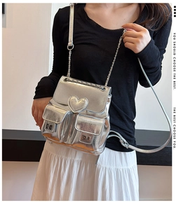 Silver metallic backpack featuring a heart detail and chain strap shown on a model