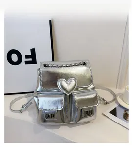 Detail of silver metallic backpack featuring a heart-shaped ornament and metal chain straps