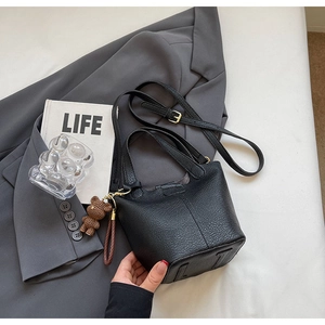 Close-up of black lychee grain leather bucket bag with golden hardware and bear charm