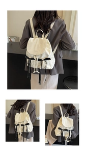 Detail showing the cream backpack with lace bows and embossed logo on the leather flap