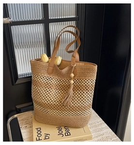Detail of woven straw tote bag with leather straps and decorative wooden bead tassels