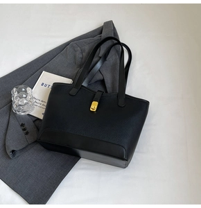 Detail of black leather tote bag featuring a gold twist-lock clasp and slim shoulder straps