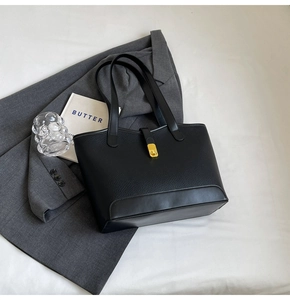 Close-up of black lychee grain leather tote bag featuring a gold metal twist lock