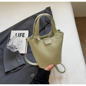 Detailed macro of a sage green litchi-grain leather bucket bag on a grey blazer suit