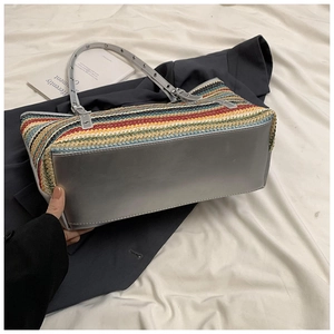 Close-up of colorful striped woven tote bag with gray faux leather base and metal buckles
