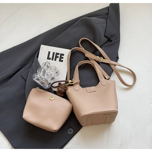 Detail of beige bucket bag with matching pouch and brown bear charm on grey fabric