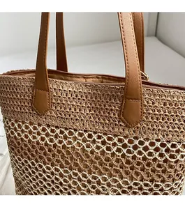 Close-up of woven straw tote bag with brown leather handles and reinforced stitching detail