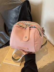 Pink canvas shell crossbody bag with floral strap and leather brand tag on table
