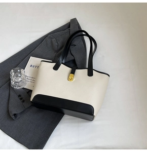 Detailed close-up of cream and black contrast tote bag with golden twist-lock buckle