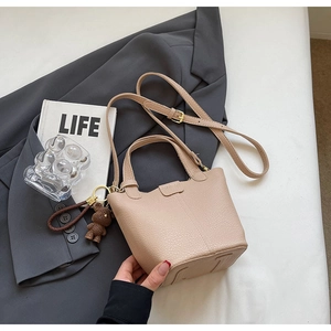 Close-up of beige leather bucket bag with litchi texture and cute bear pendant charm