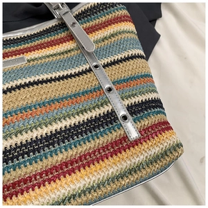 Detailed macro view of colorful woven stripes and metal logo plate on a straw tote bag