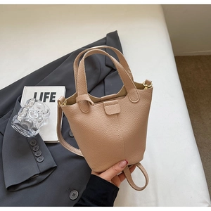 Close-up of litchi pattern leather bucket bag placed on a grey suit with a book