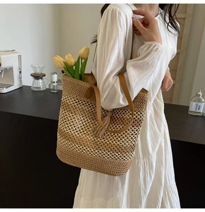 Detail of hand-woven straw tote with hollow mesh pattern and leather tassel charm