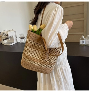 Detail of straw woven tote bag with white grid pattern, brown leather strap and tassel charm