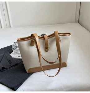 Close-up of cream canvas tote bag with brown leather trim and golden metal turn-lock