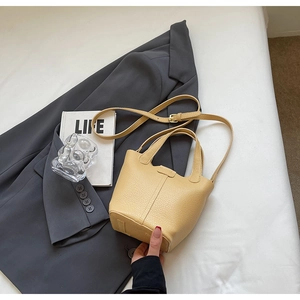 Close-up of pale yellow litchi grain leather bucket bag with dual handles and strap
