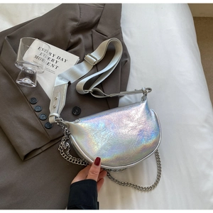 Détail du sac selle laser iridescent avec chaîne en métal sur fond de costume brun