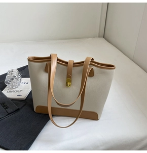 Detail view of large canvas tote bag with brown leather trim and golden metal lock