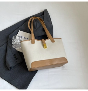 Detail of contrast stitching and golden twist lock on a beige lychee leather tote bag
