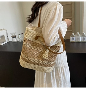 Detail of a large woven straw tote bag featuring contrast stitching and leather tassel