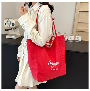 Detail of red canvas tote bag with beyou merci print and striped handles