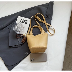 Close-up of light yellow lychee pattern leather bucket bag with plush bear charm