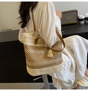 Detail of gradient woven straw tote bag featuring long fringes and brown leather straps