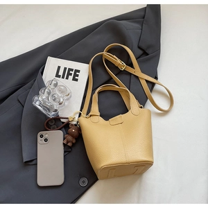 Detail of ginger yellow bucket bag with litchi grain leather and cute bear charm