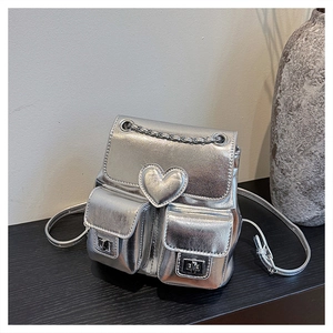 Detail of silver metallic mini backpack featuring heart-shaped stitching and buckle pockets