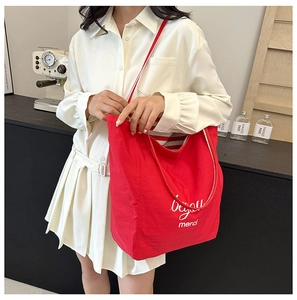 Detail of red canvas tote bag with white beyond lettering shown on a female model