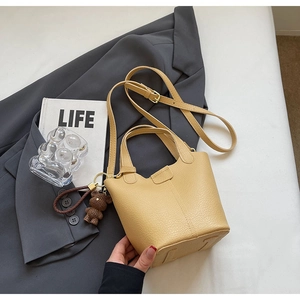 Close-up of beige leather bucket bag with woven bear charm and adjustable shoulder strap