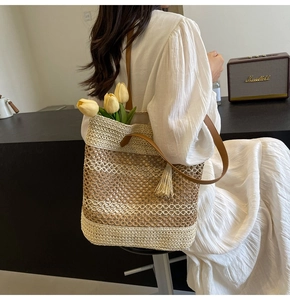 Detail of woven straw tote bag featuring brown leather straps and a decorative tassel