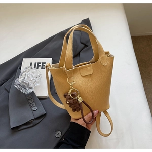 Detailed shot of yellow bucket bag with textured leather and a brown knit bear charm