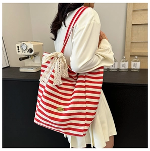 Detail of canvas tote bag showing red striped pattern and large lace bow decoration
