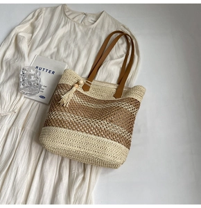 Close-up of a striped straw tote bag with leather handles and beige fringe on white dress