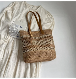 Close-up of woven straw tote bag with wave pattern, leather handles, and wood bead tassel