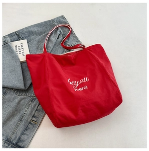 Close-up of red canvas tote bag with 'be you merci' print and striped ribbon handles