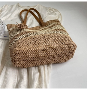 Detail of woven straw tote bag featuring two-tone stripes and brown leather handles