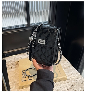 Detail of glossy black quilted mini bag with silver twist lock and chain strap