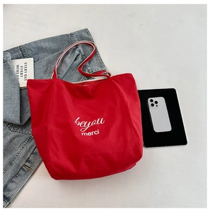 Detail of red canvas tote bag featuring white artistic lettering and striped handles