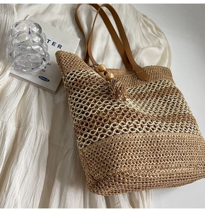 Detail of woven straw tote bag with brown leather handles and decorative tassel ornament